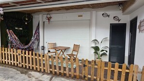 A white building with a wooden fence, a hammock, a table, and two chairs outside.