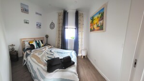 A bedroom with a bed, a bedside table, a lamp, a window with curtains, and wall art.