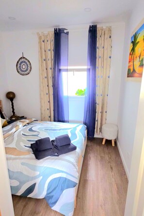 A bedroom with a bed, curtains, a small stool, and a wall decoration.