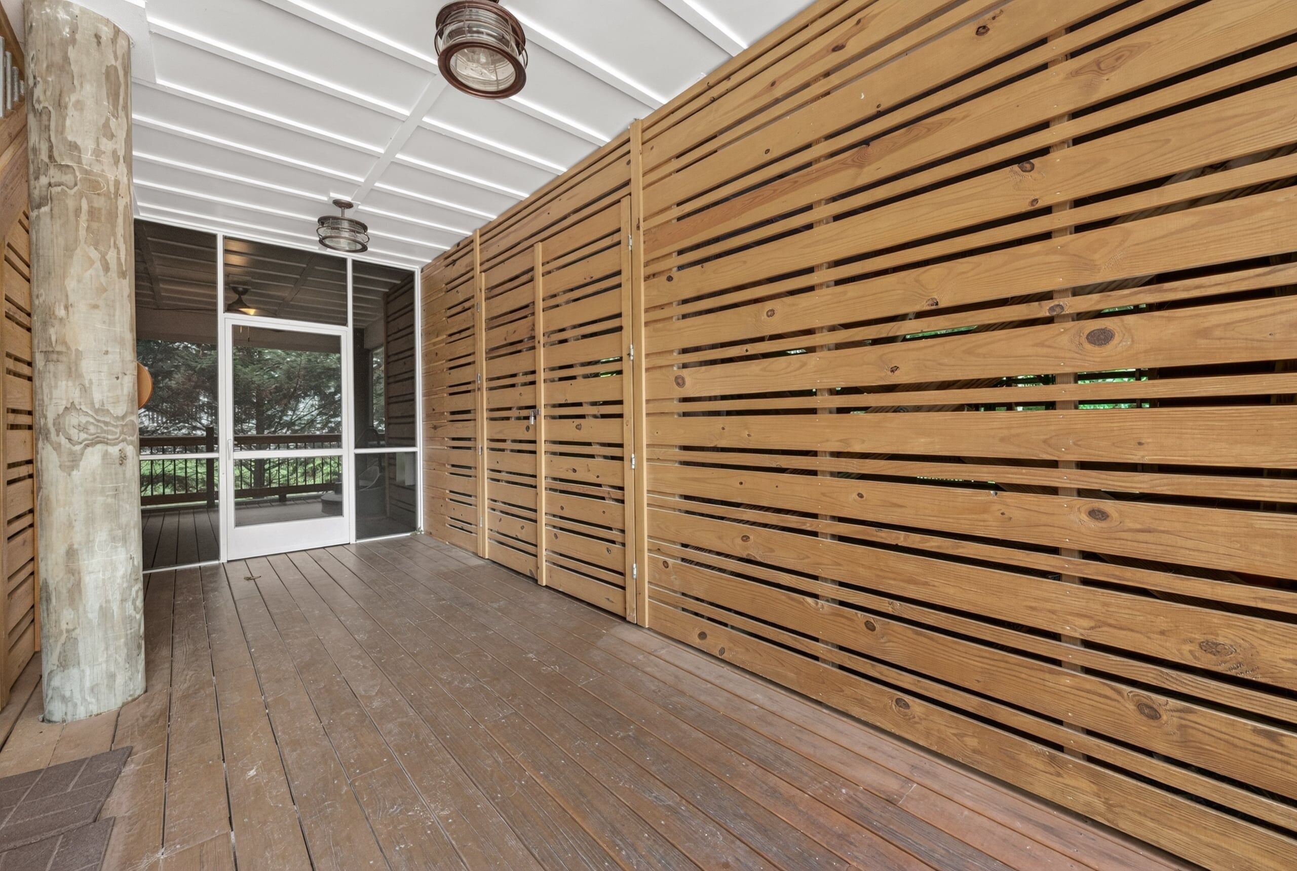 A wooden deck with a ceiling and a glass door leading outside.