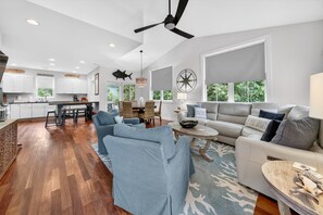 A spacious living area with a large sofa, a dining table, and a kitchen in the background. - Pawleys Hideaway On The Causeway 3 Bedroom Home (Pawleys Island)