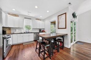 A modern kitchen with white cabinets, a wooden island with bar stools, and a large window. - Pawleys Hideaway On The Causeway 3 Bedroom Home (Pawleys Island)