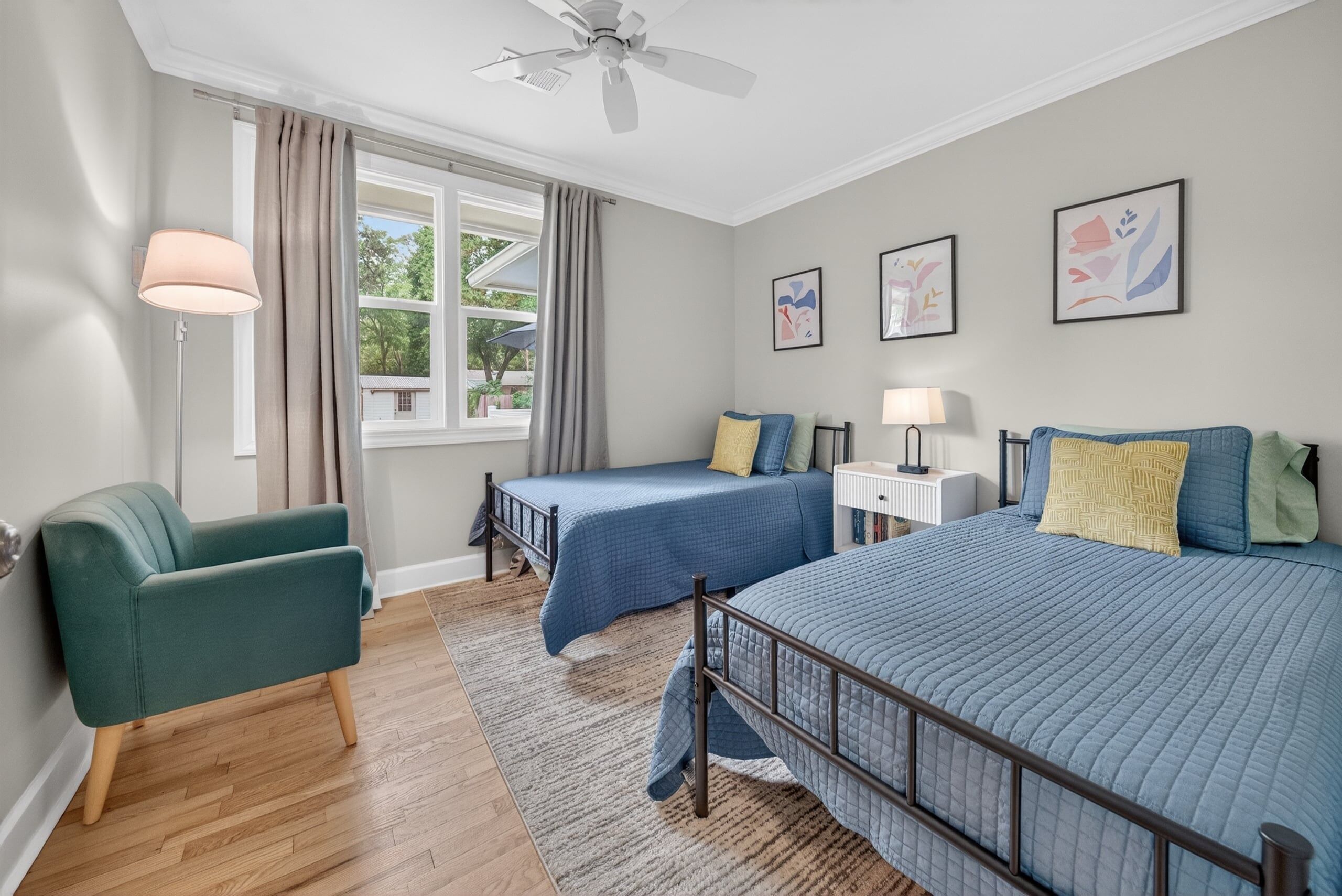 A bedroom with two beds, a chair, a desk, and a window with curtains.