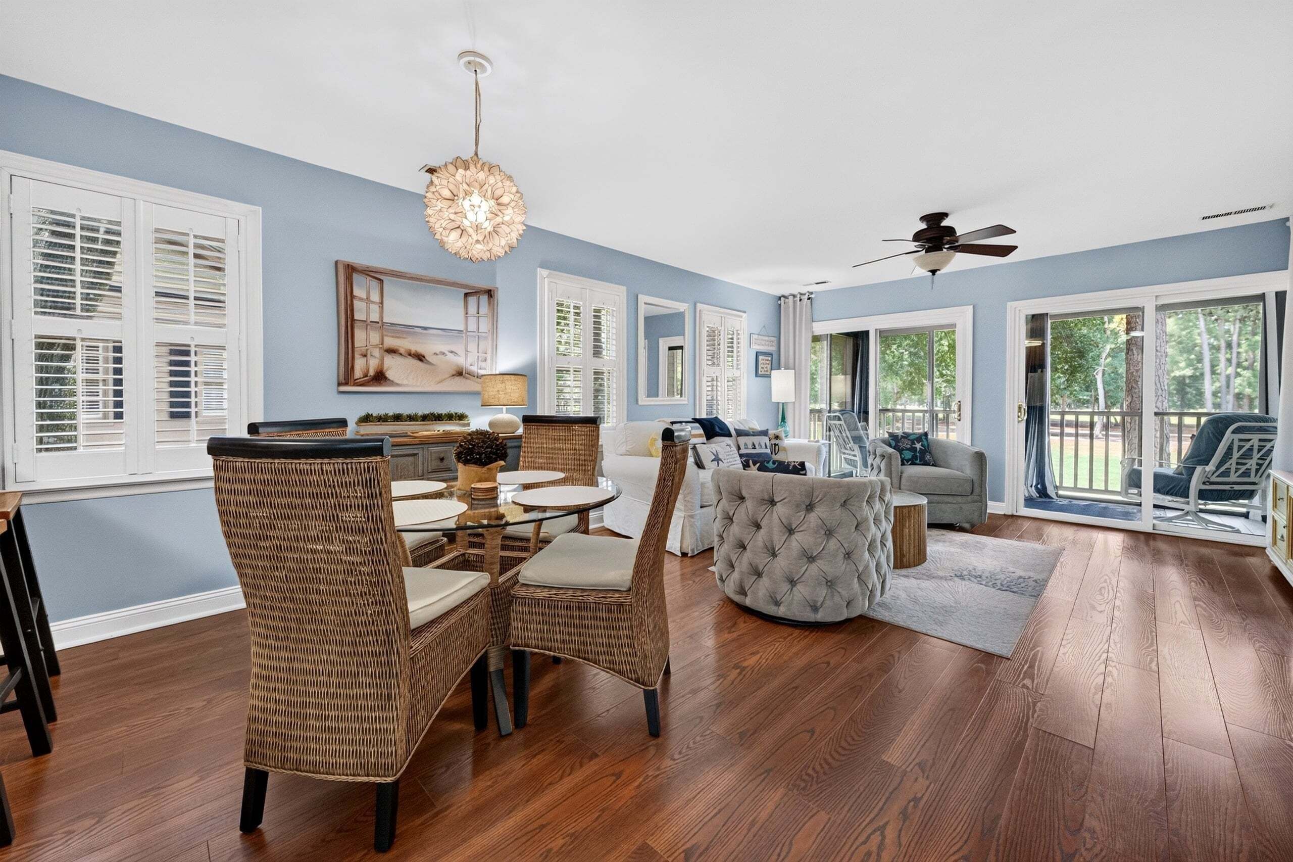 A spacious living room with a dining area, large windows, and a ceiling fan.