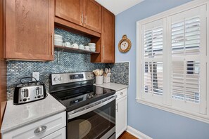A kitchen with wooden cabinets, a toaster, an oven, and a window with blinds. - 127-3 Puttin On The Ritz 2 Bedroom Condo (Pawleys Island)