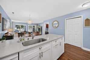 A modern kitchen with a large island, stainless steel appliances, and a view into the living area. - 127-3 Puttin On The Ritz 2 Bedroom Condo (Pawleys Island)