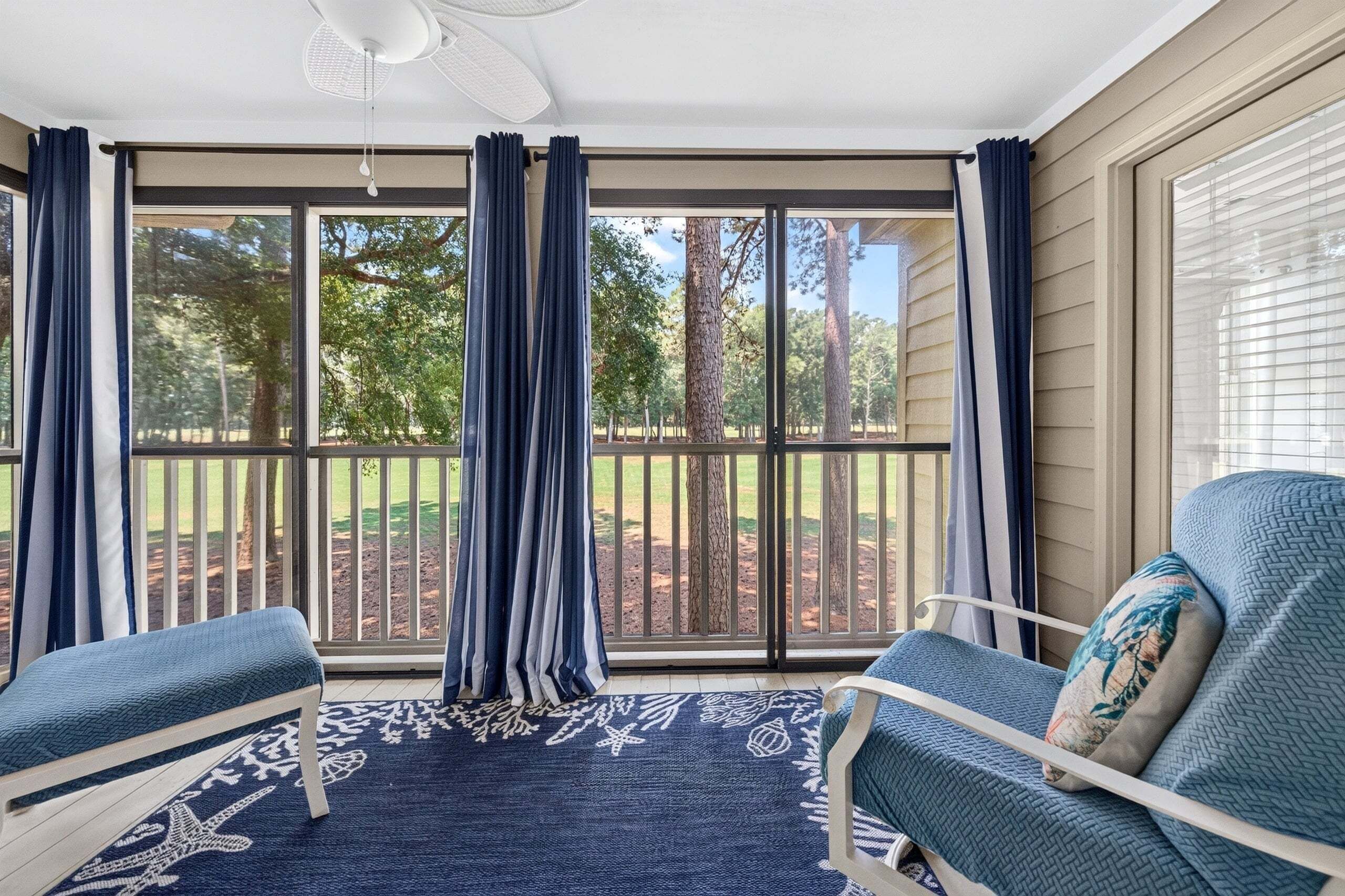 A sunroom with a large sliding glass door, two chairs, a patterned rug, and a ceiling fan.