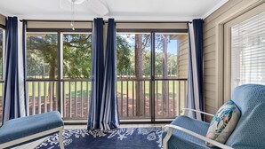 A sunroom with a large sliding glass door, two chairs, a patterned rug, and a ceiling fan. - 127-3 Puttin On The Ritz 2 Bedroom Condo (Pawleys Island)