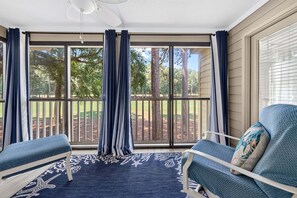 A sunroom with a large sliding glass door, two chairs, a patterned rug, and a ceiling fan. - 127-3 Puttin On The Ritz 2 Bedroom Condo (Pawleys Island)