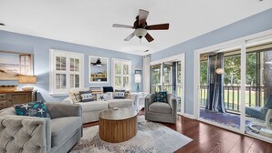 A spacious living room with a ceiling fan, large windows, and a view of the outdoors. - 127-3 Puttin On The Ritz 2 Bedroom Condo (Pawleys Island)