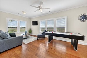 Una sala de estar con mesa de billar, sofá, ventilador de techo y ventanas amplias.