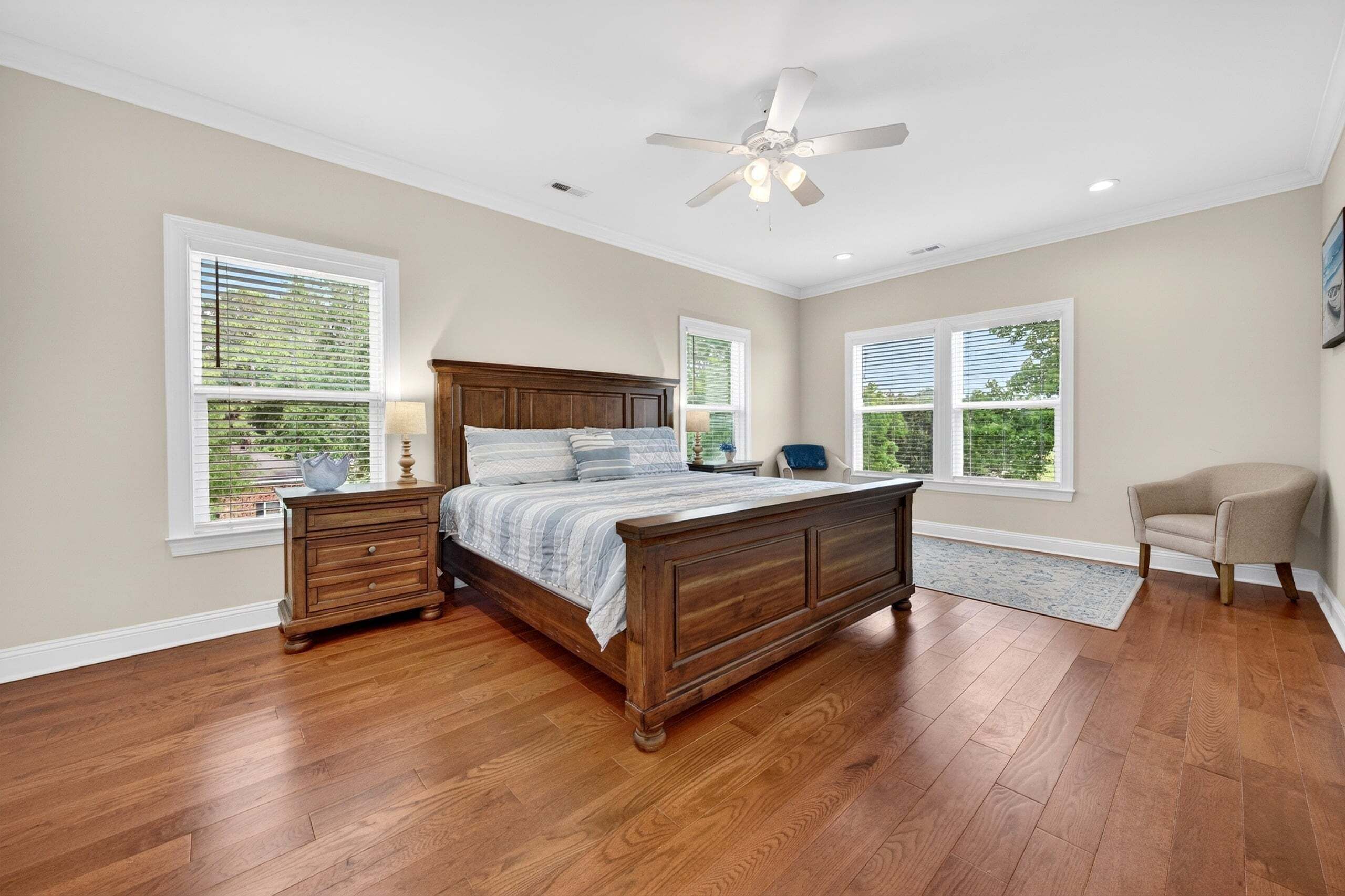 A bedroom with a wooden bed, two nightstands, a ceiling fan, and large windows with blinds.