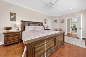 Un dormitorio con cama de madera, mesitas de noche, ventilador de techo y obras de arte en las paredes.