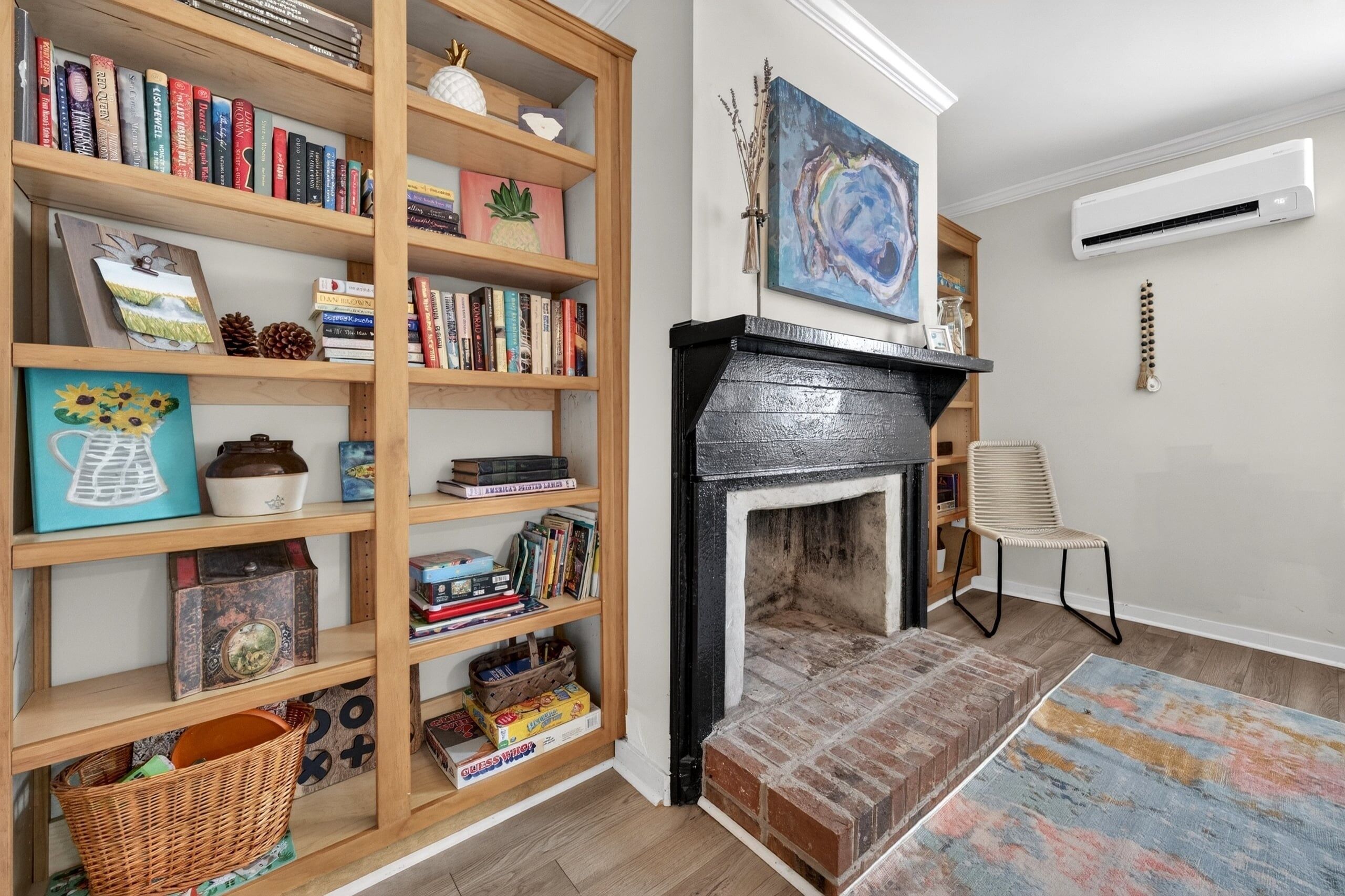 Une pièce avec une bibliothèque, une cheminée, un fauteuil et un tableau au mur.