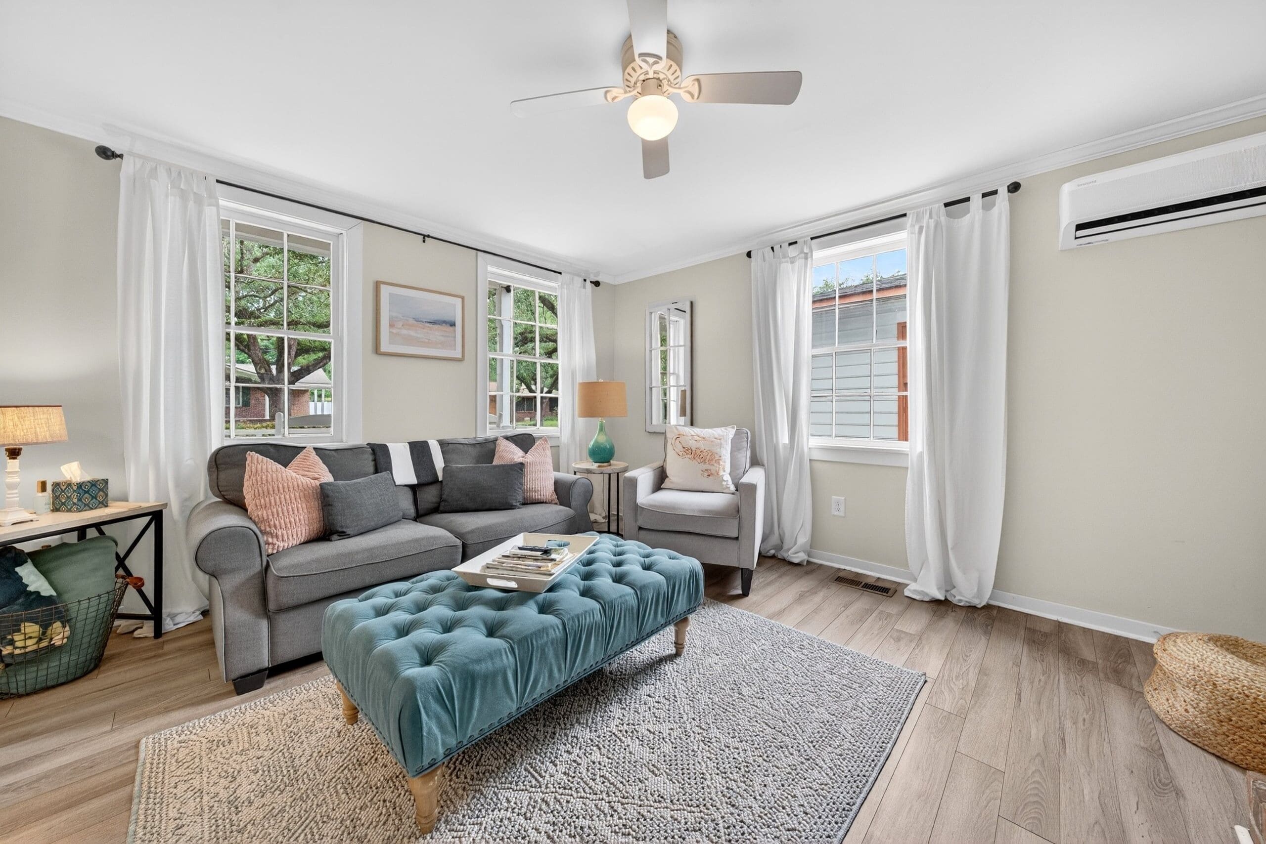A living room with a grey sofa, a blue ottoman, a side table with a lamp, and a ceiling fan.
