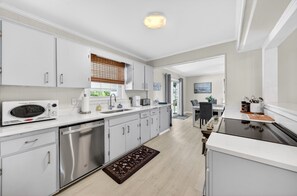 A modern kitchen with white cabinetry, stainless steel appliances, and a wooden floor. - Charming Coastal Retreat 3 Bedroom Home (Georgetown)