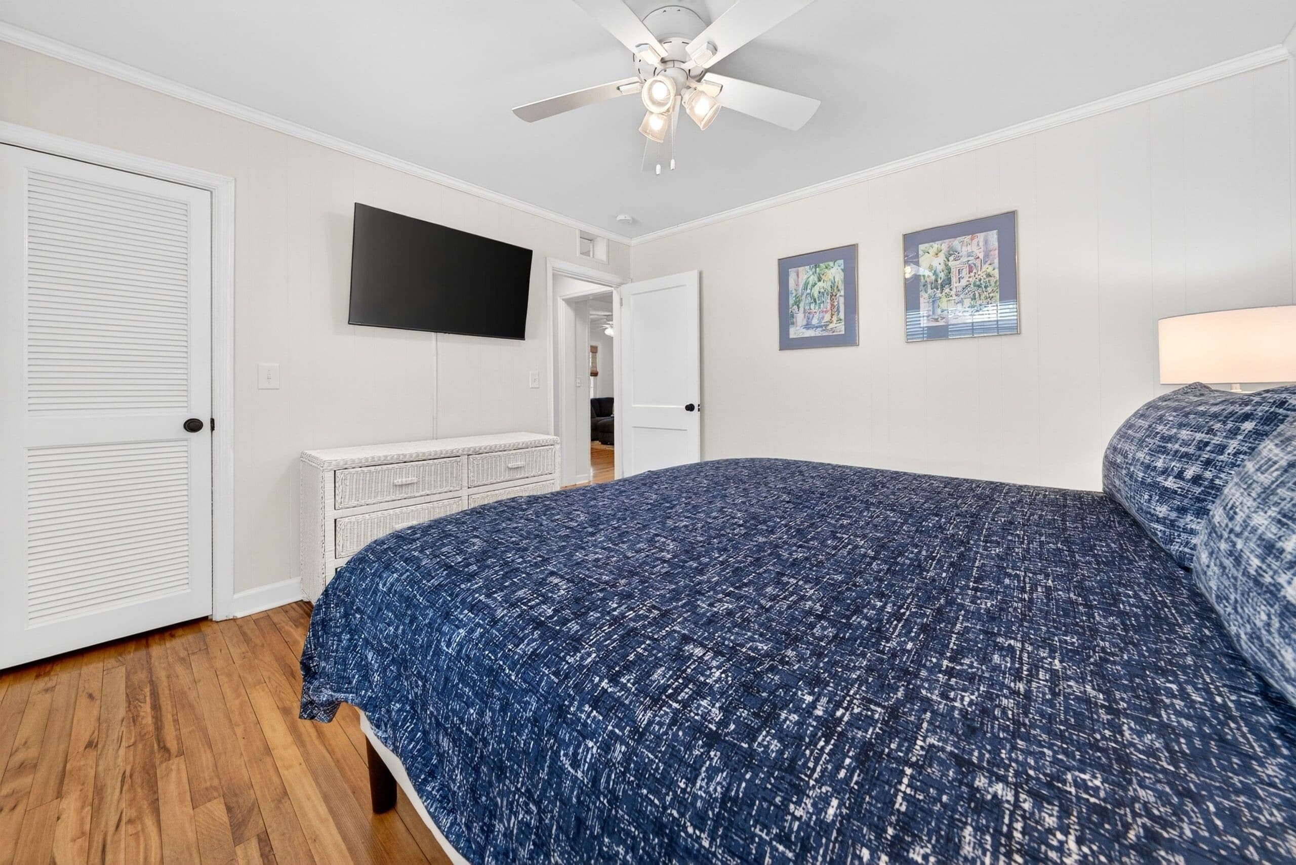 A bedroom with a bed, a ceiling fan, a TV, and two framed pictures on the wall.