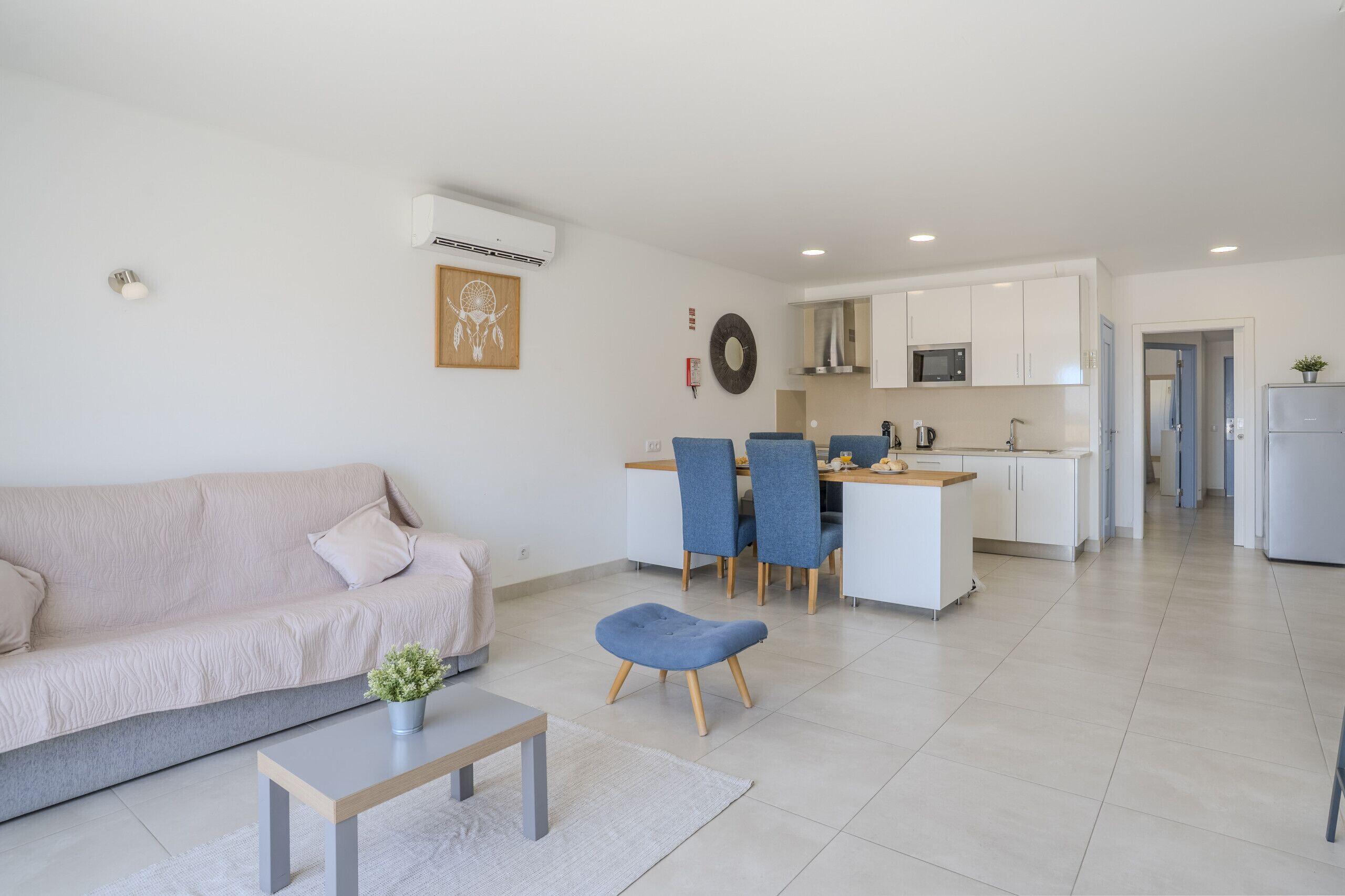 A modern living room with a sofa, a coffee table, and a dining area with chairs and a kitchen in the background.