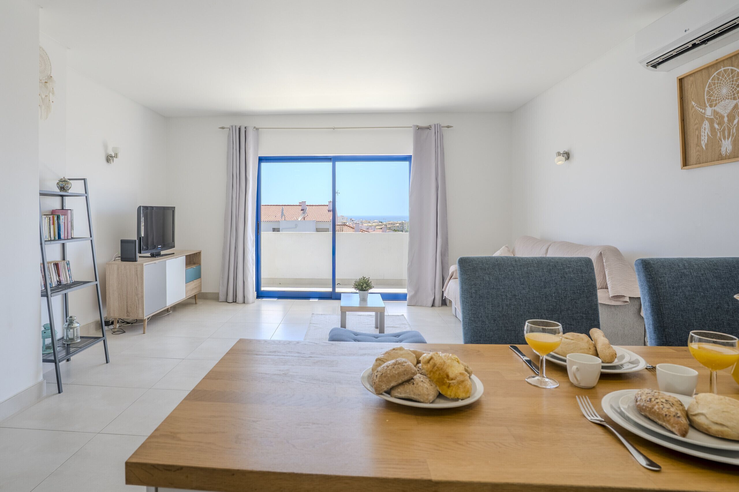 A modern living room with a dining table set for breakfast, a sofa, a TV, and a bookshelf.