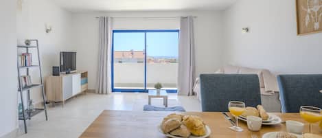 Een moderne woonkamer met een ontbijt klaar dektafel, een bank, een televisie en een boekenkast.