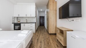 A modern hotel room with a kitchenette, a bed with neatly folded white towels, a wooden wardrobe, and a flat-screen TV mounted on the wall. - Sea Stay Studio Durr s Waterfront (Durrës)