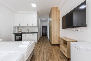 A modern hotel room with a kitchenette, a bed with neatly folded white towels, a wooden wardrobe, and a flat-screen TV mounted on the wall. - Sea Stay Studio Durr s Waterfront (Durrës)