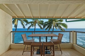 Een balkon met een tafel en stoelen, met uitzicht op de oceaan met palmbomen.
