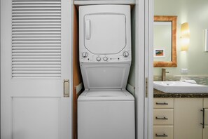 Un lavadero compacto con lavadora y secadora integradas, un lavabo con encimera de granito y un espejo sobre el lavabo.
