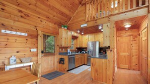 L’intérieur d’un chalet en bois comprend une cuisine, un coin repas et un escalier menant à un niveau supérieur.