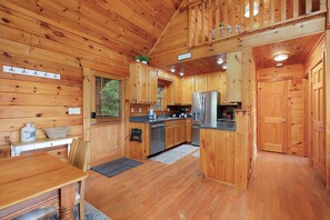 Ein Holzblockhaus-Innenraum mit Küche, Essbereich und einer Treppe, die zu einer oberen Ebene führt.