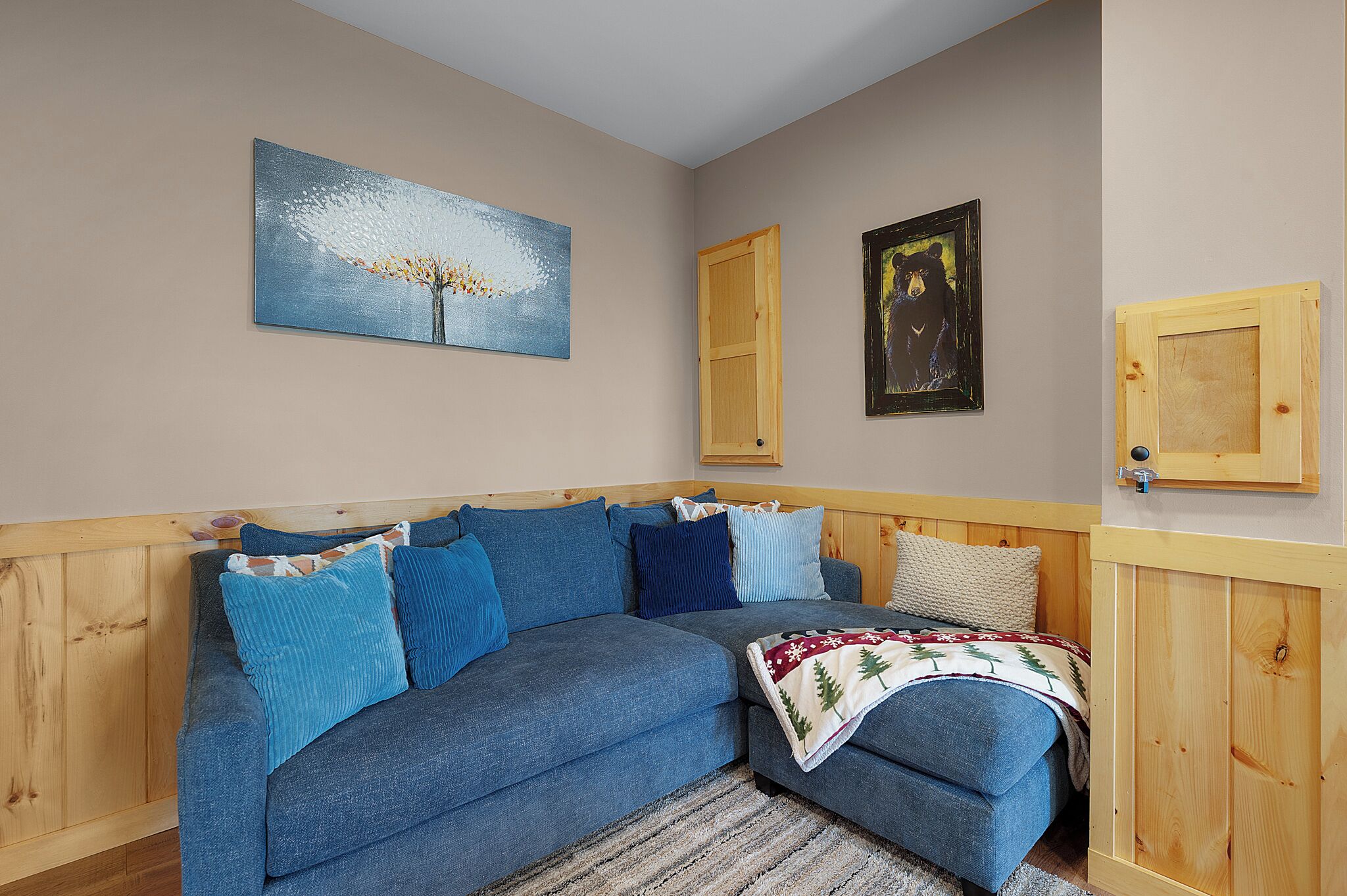Una habitación con sofá azul, paneles de madera, un cuadro de un árbol y una foto enmarcada de un oso.