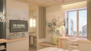 A hotel room with a bed, a desk, a window with a view, a wall-mounted TV, and a bathroom visible through an open door. - THE MEADOW Gronau by Hackmann (Gronau (Westphalia))