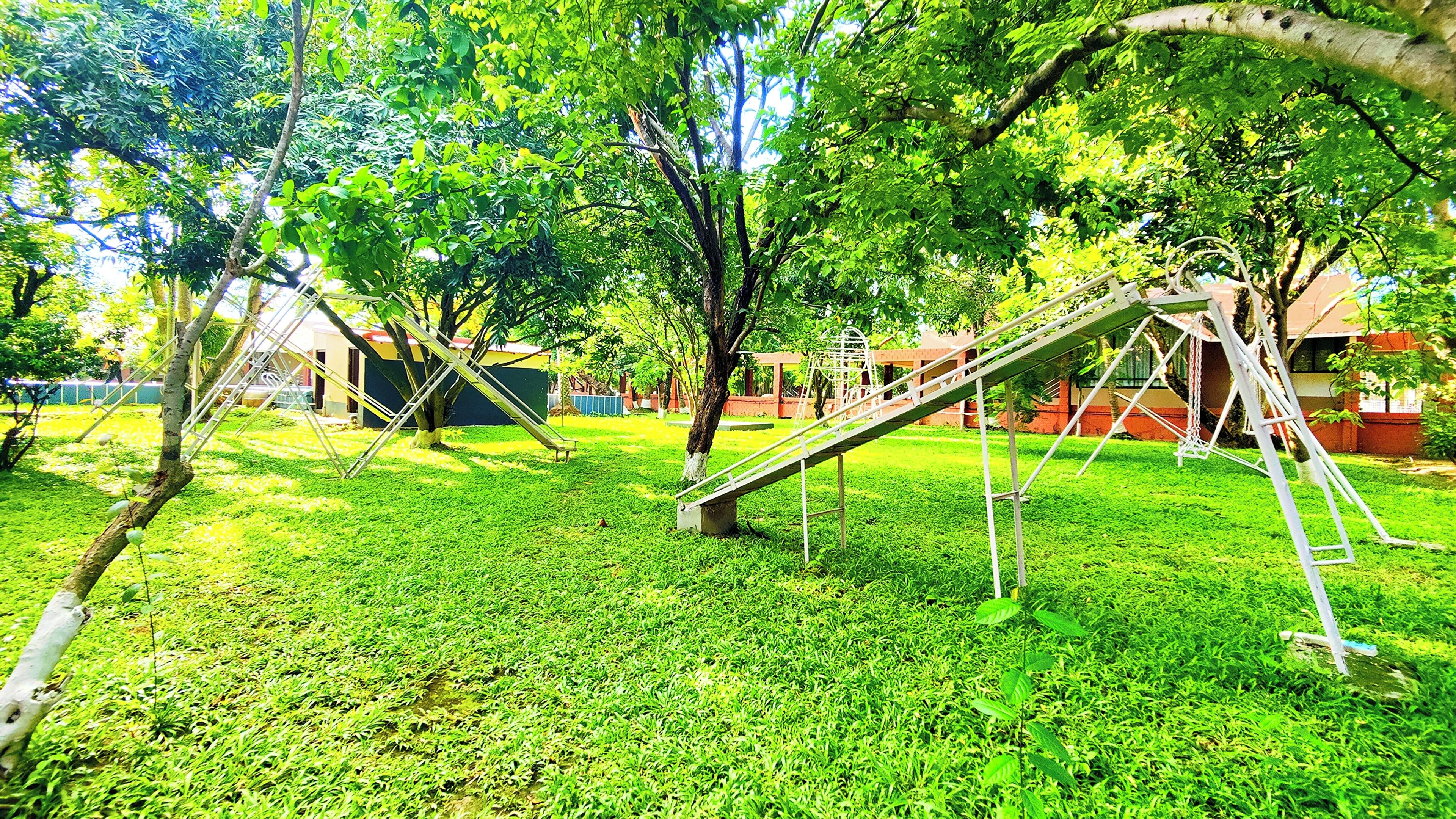Ein Spielplatz mit Schaukeln und Rutschen, umgeben von Gras und Bäumen.