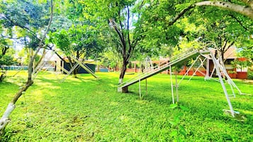 Ein Spielplatz mit Schaukeln und Rutschen, umgeben von Gras und Bäumen.