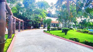 A paved pathway leading to a building with a modern design, surrounded by lush greenery and palm trees. - Mark & Meadows (Bolpur)