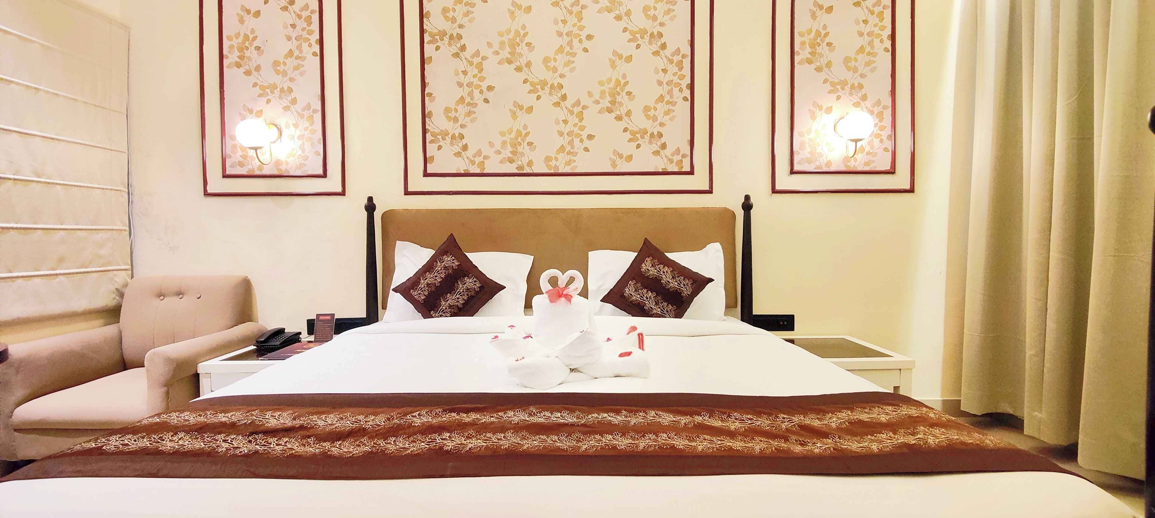 A hotel room with a bed, a chair, a bedside table, and wall-mounted lights.