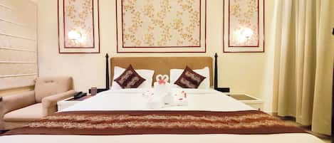 Una habitación de hotel con cama, una silla, una mesita de noche e iluminación en la pared.