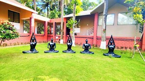 A courtyard with five black yoga statues on grass, surrounded by buildings with red and beige walls. - Mark & Meadows (Bolpur)