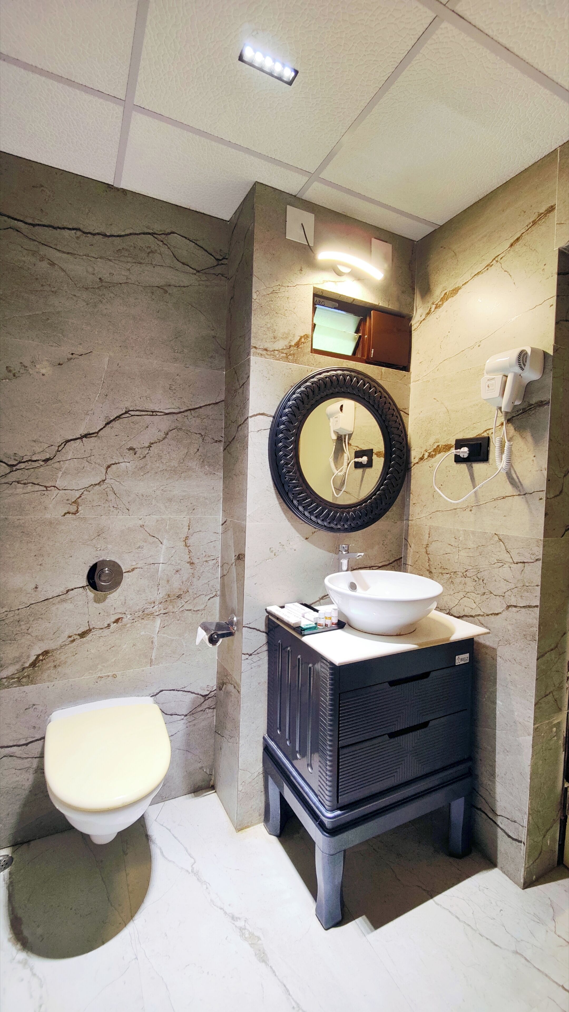A bathroom with a marble wall, a sink, a toilet, and a mirror.