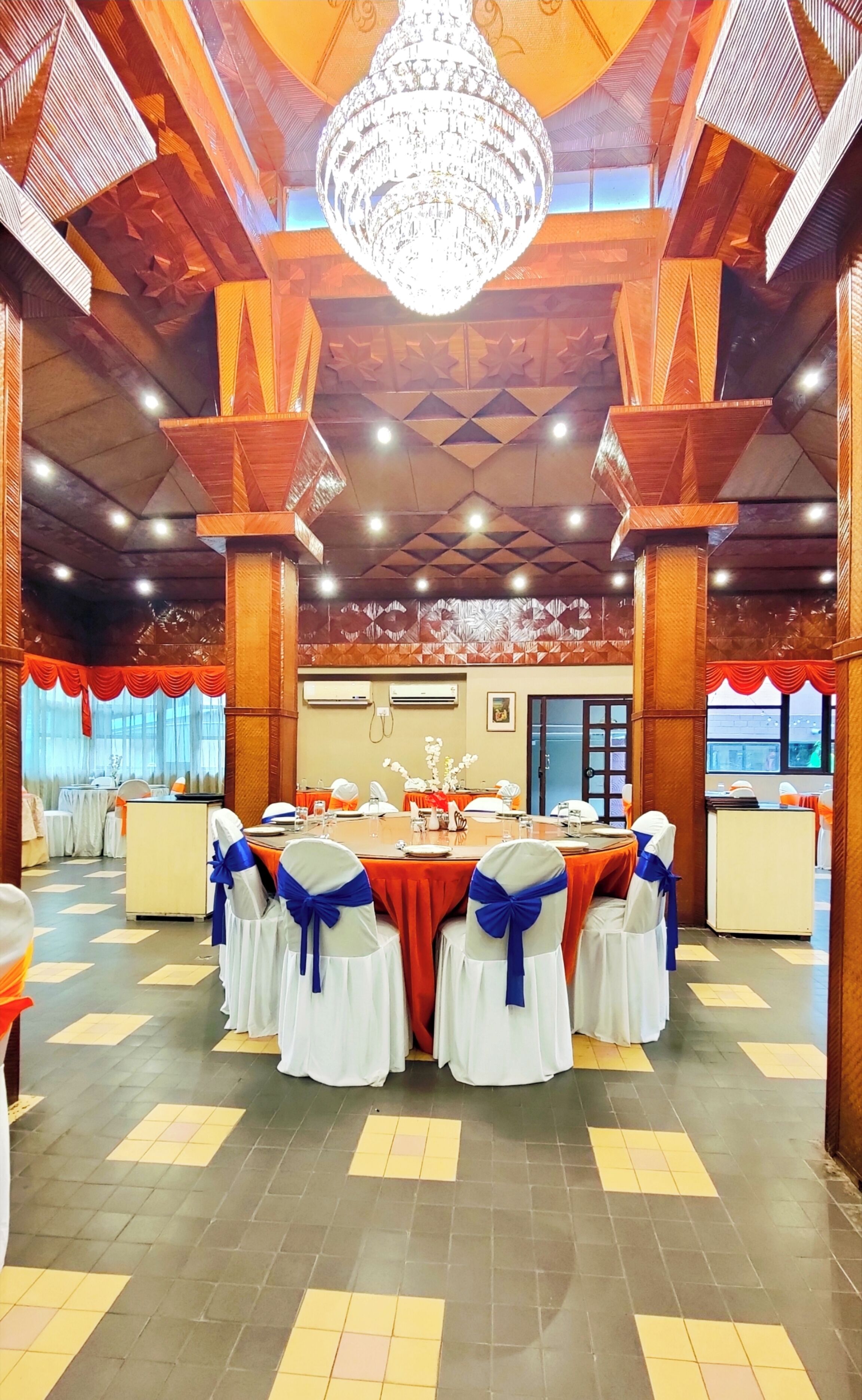 Un salón de banquetes con una larga mesa, sillas blancas adornadas con cintas azules y una araña.