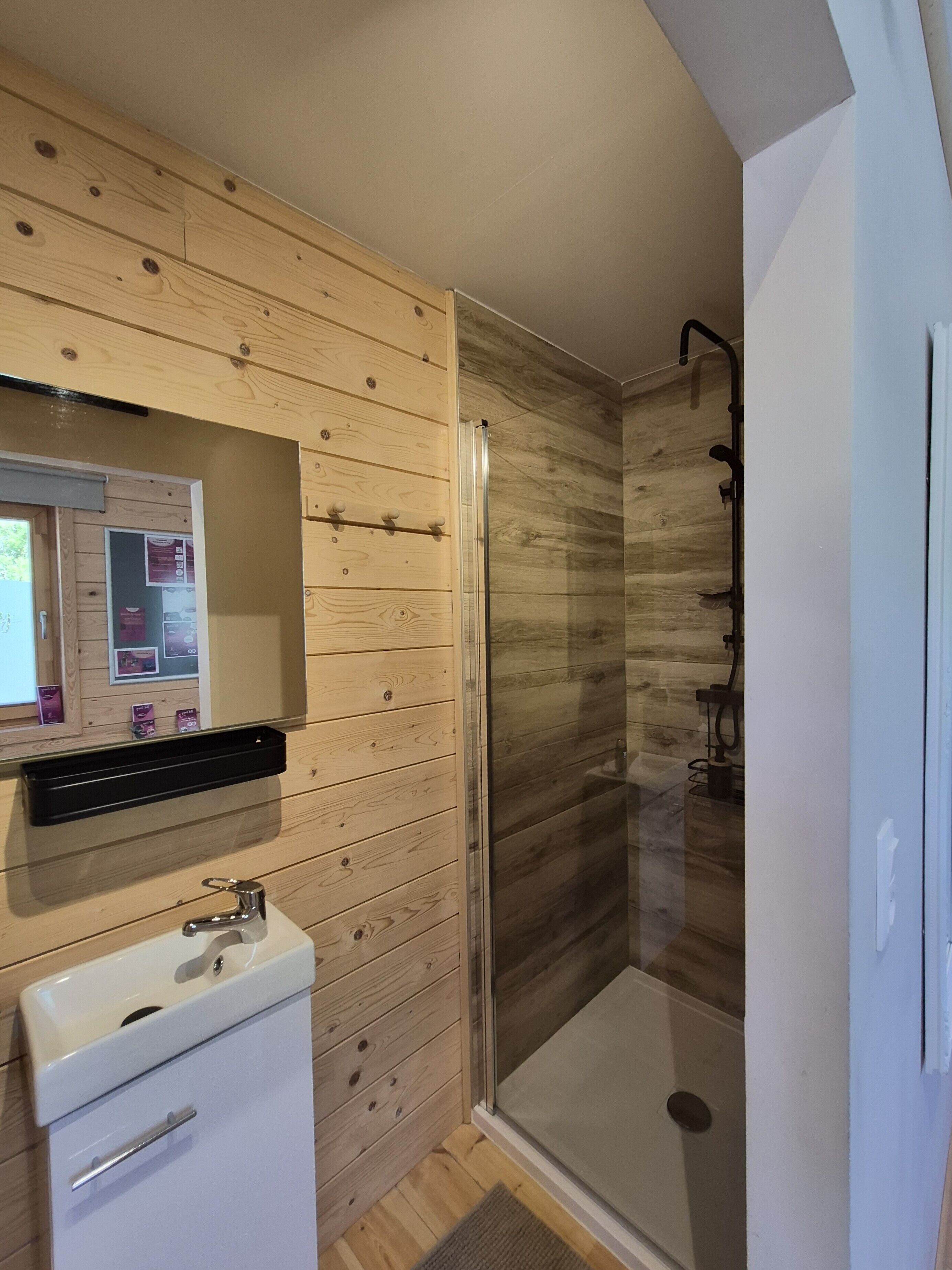 A bathroom with wooden paneling, a sink, and a glass shower enclosure.