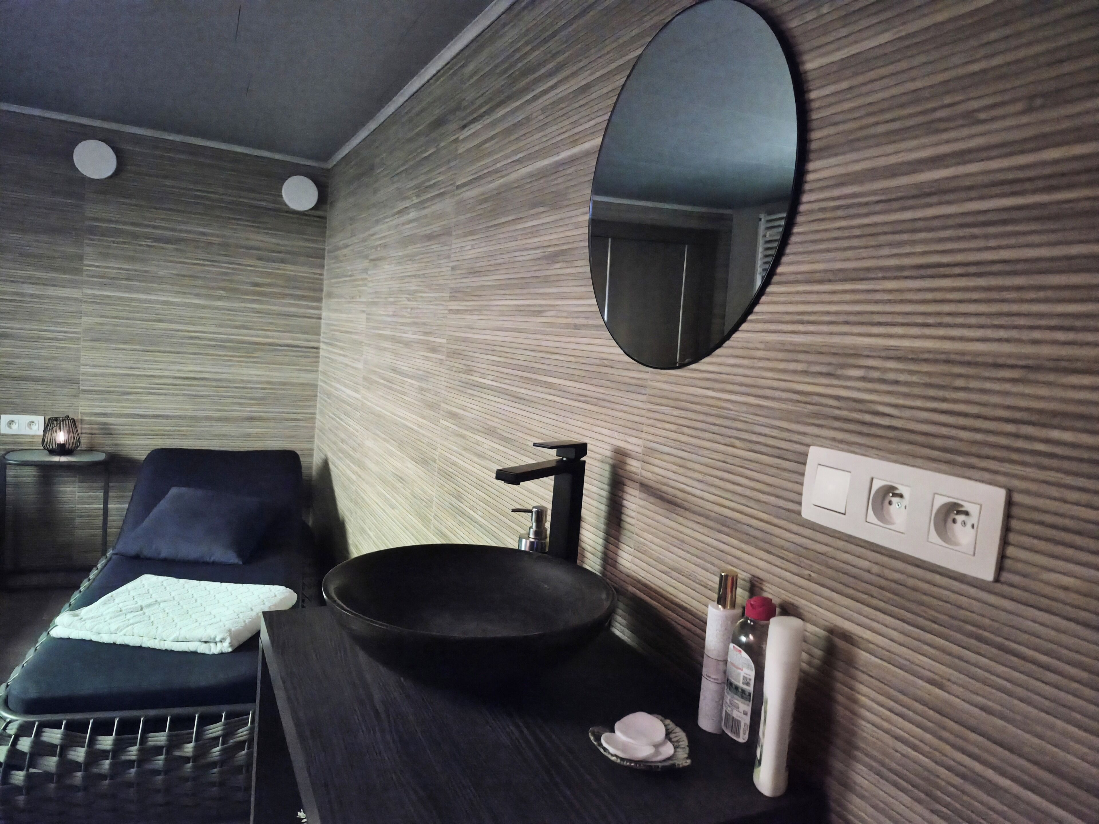 Une salle de bain moderne avec un lavabo noir, un miroir rond, une serviette et une petite assiette posée sur le comptoir.