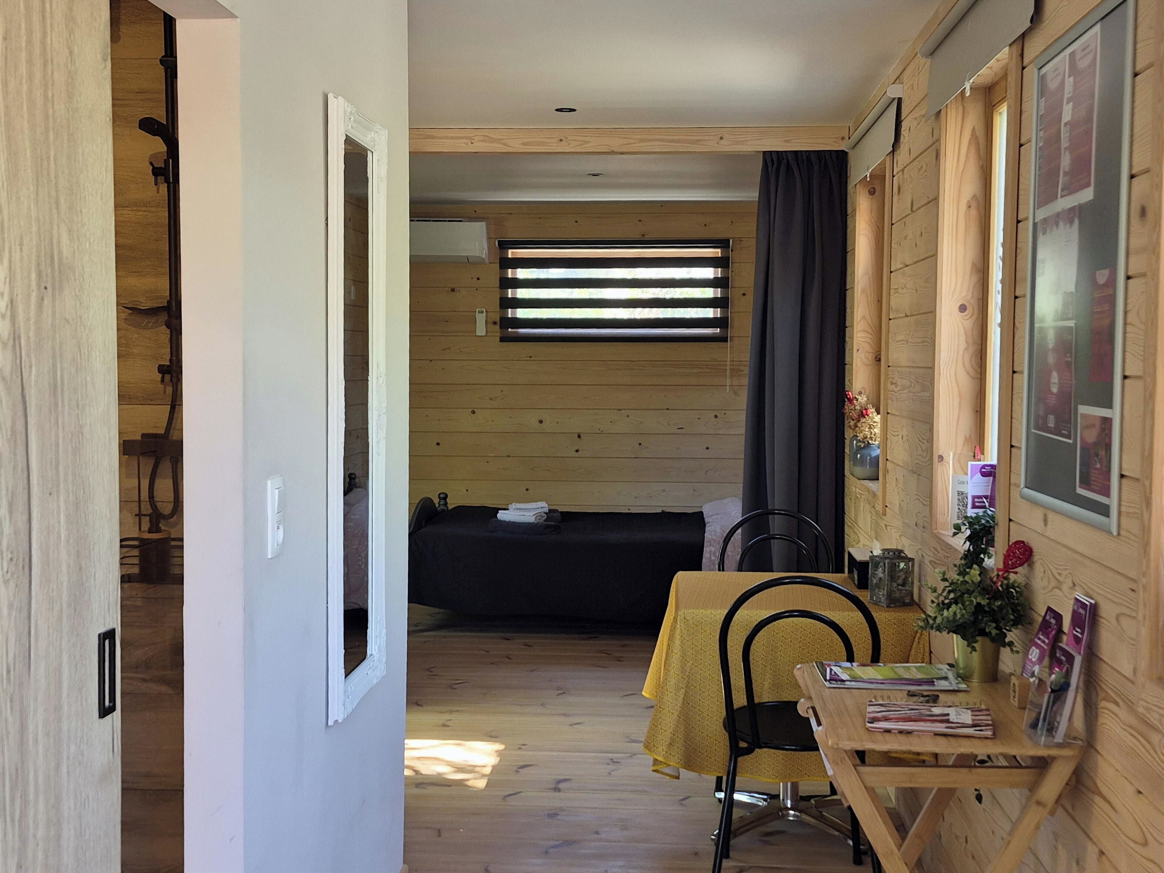 Een kleine kamer met een bed, een tafel met stoel en een raam met zonwering.