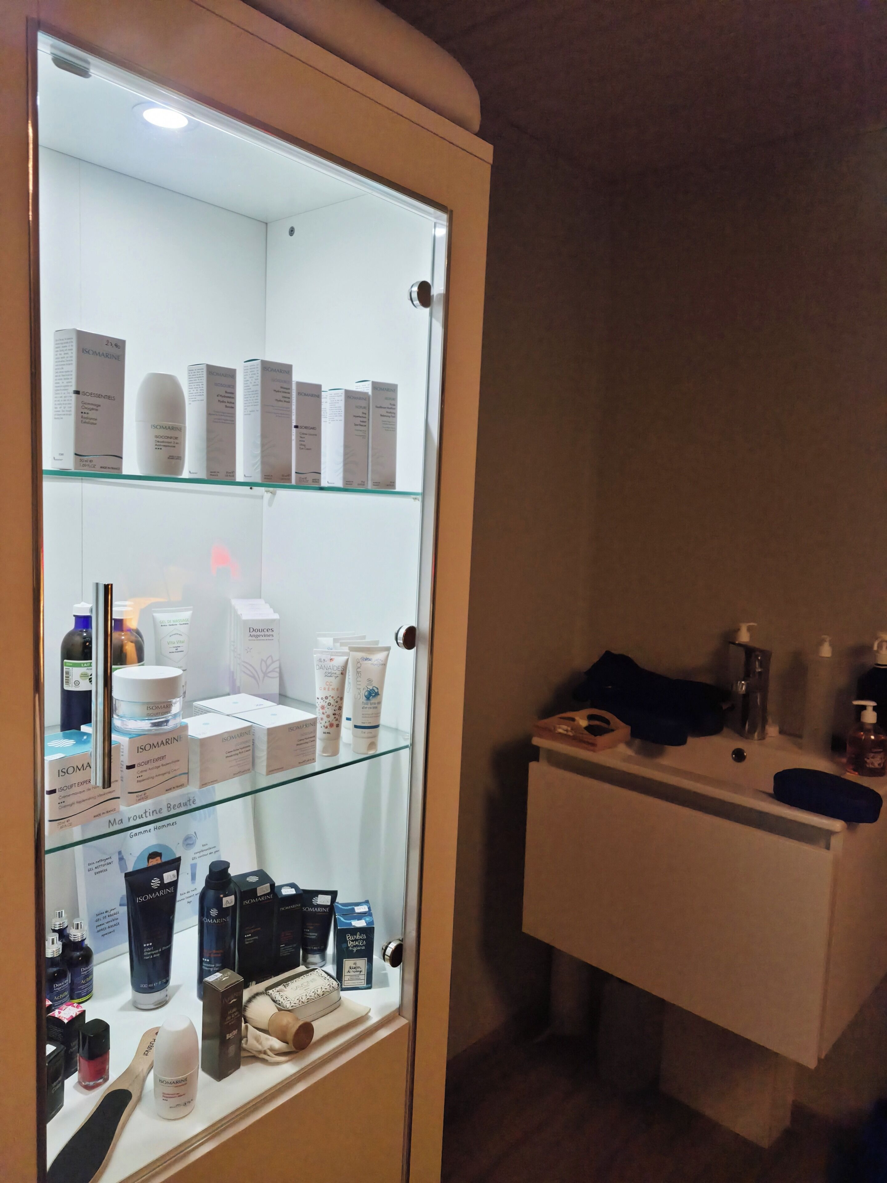 Une vitrine avec une façade en verre, où sont exposés divers produits de soins pour la peau, un banc en bois et un comptoir blanc où sont présentés des articles de toilette.