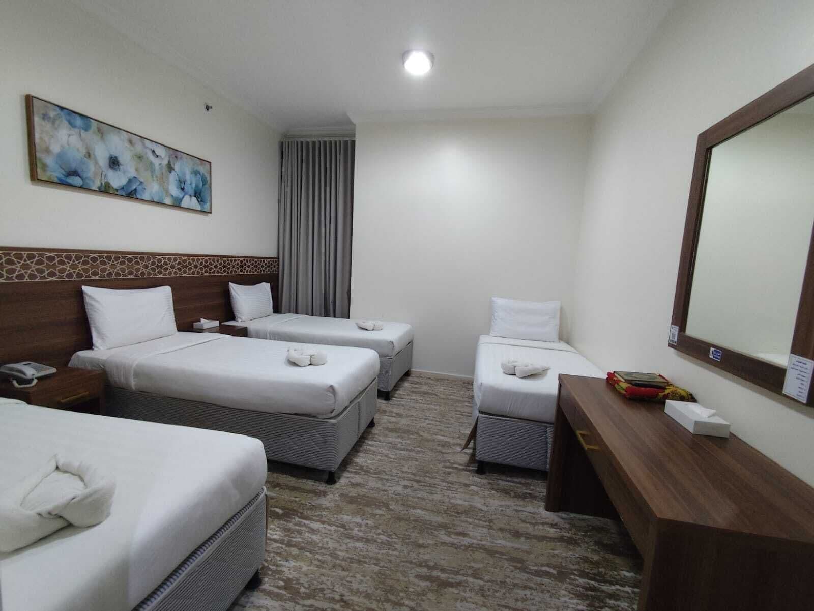 A hotel room with two beds, a desk, a mirror, and a painting on the wall.