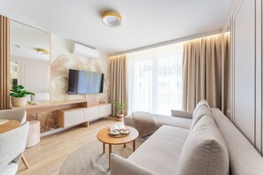 Ein modernes Wohnzimmer mit einer Couch, einem Couchtisch, einem Fernseher und einem großen Fenster mit Vorhängen.