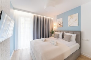 Ein modernes Hotelzimmer mit einem großen Bett, einem Flachbildfernseher, einem Fenster mit Vorhängen und zwei an der Wand befestigten Kunstwerken.