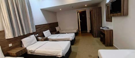 A hotel room with four single beds, a TV mounted on the wall, and a wooden headboard.
