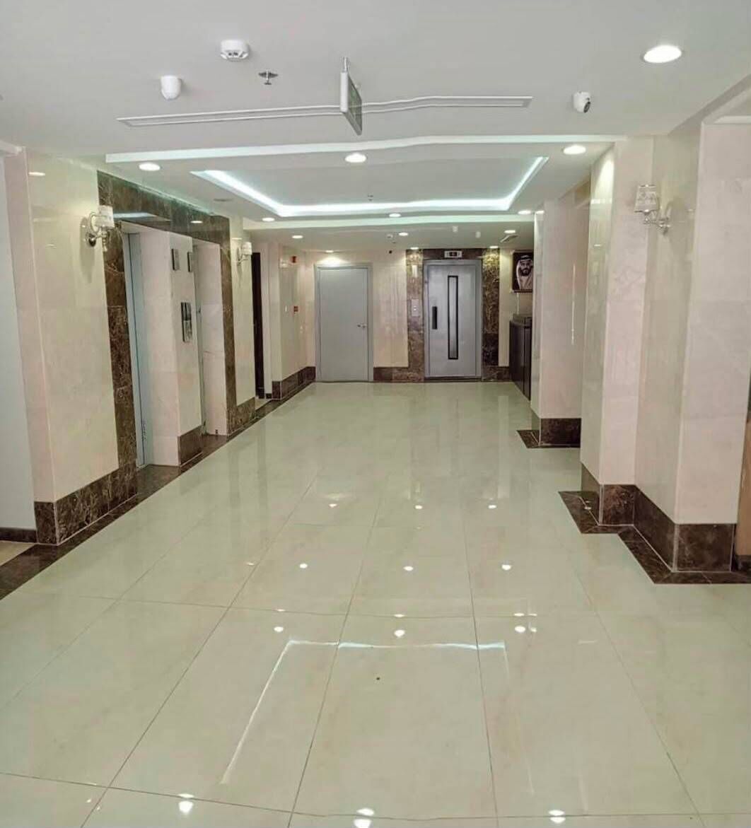 A hotel corridor with a shiny tiled floor, recessed lighting, and a door at the end.