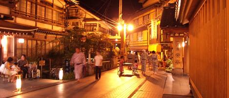 Una calle tradicional japonesa de noche con gente caminando y edificios históricos.